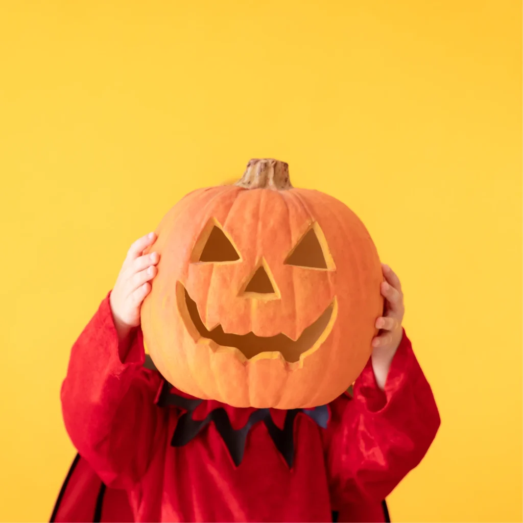 child holding pumkin for halloween over his face on a yellow background